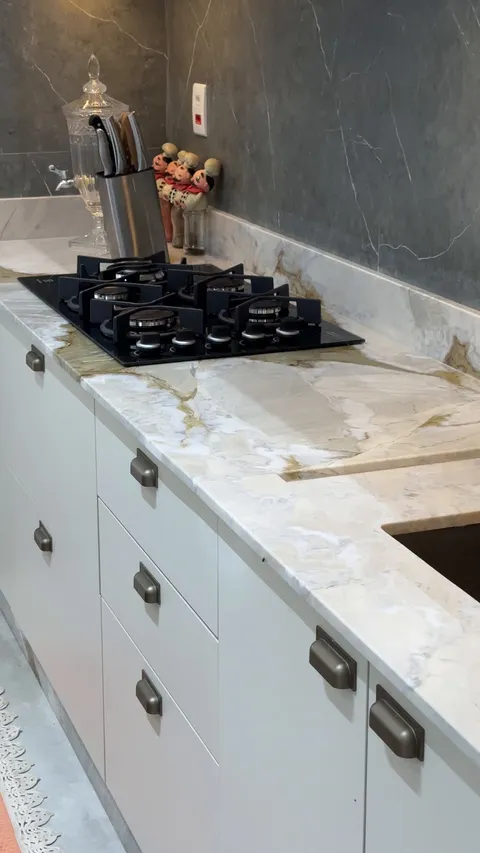 Bancada em quartzito com cooktop embutido, saia slim e rodabanca na mesma pedra.